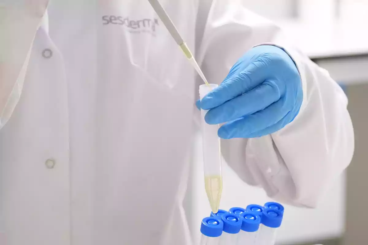Investigador con guantes azules manipulando una pipeta y un tubo de ensayo en un laboratorio.