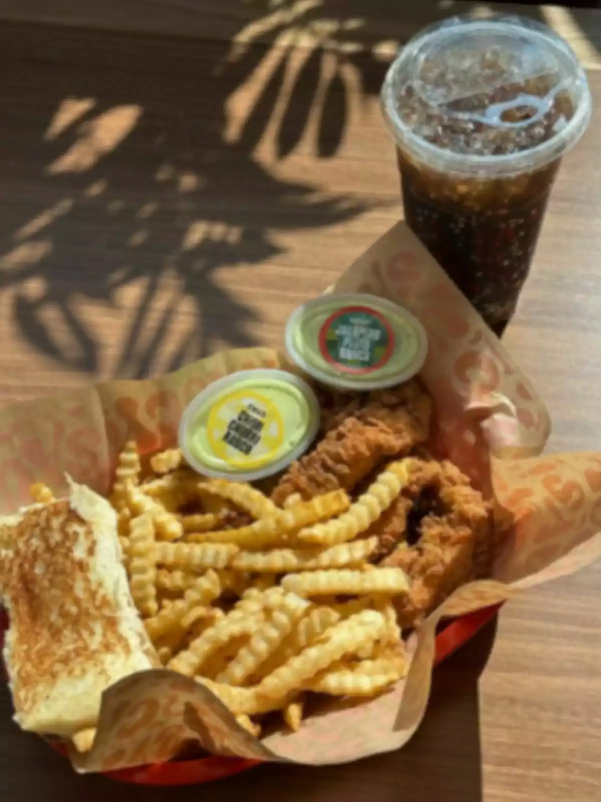 A fast food plate with French fries, Saucy breaded chicken, toasted bread, two sauces, and a soda in a lidded cup on a wooden table. A fast food plate with French fries, Saucy breaded chicken, toasted bread, two sauces, and a soda in a lidded cup on a wooden table.