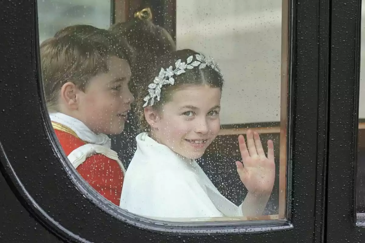 Dos niños sonrientes dentro de un carruaje saludan a través de una ventana con gotas de lluvia. Dos niños sonrientes dentro de un carruaje saludan a través de una ventana con gotas de lluvia.