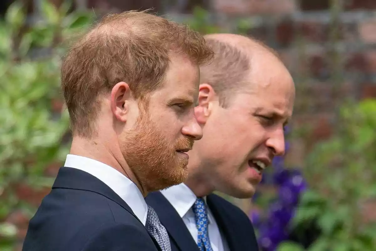 Two men in profile dressed in dark suits and ties, in an outdoor setting with vegetation in the background. Two men in profile dressed in dark suits and ties, in an outdoor setting with vegetation in the background.