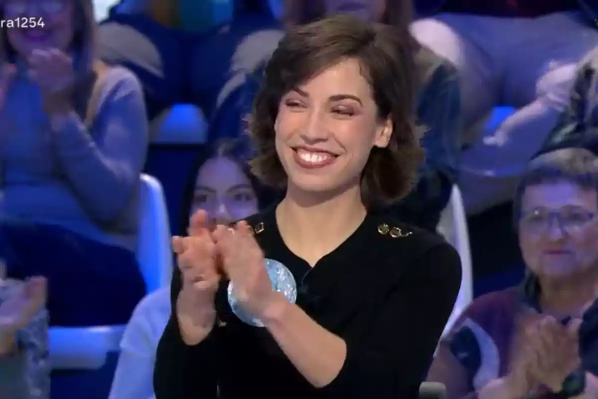 Rosa sonriente aplaude en un programa de televisión con público en el fondo. Rosa sonriente aplaude en un programa de televisión con público en el fondo.