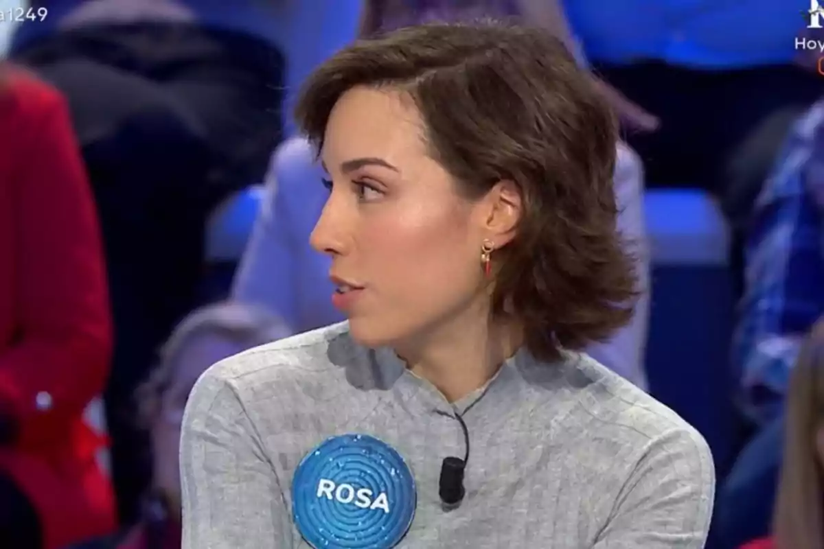 Rosa con cabello corto y castaño lleva un micrófono y un distintivo azul con el nombre Rosa con cabello corto y castaño lleva un micrófono y un distintivo azul con el nombre