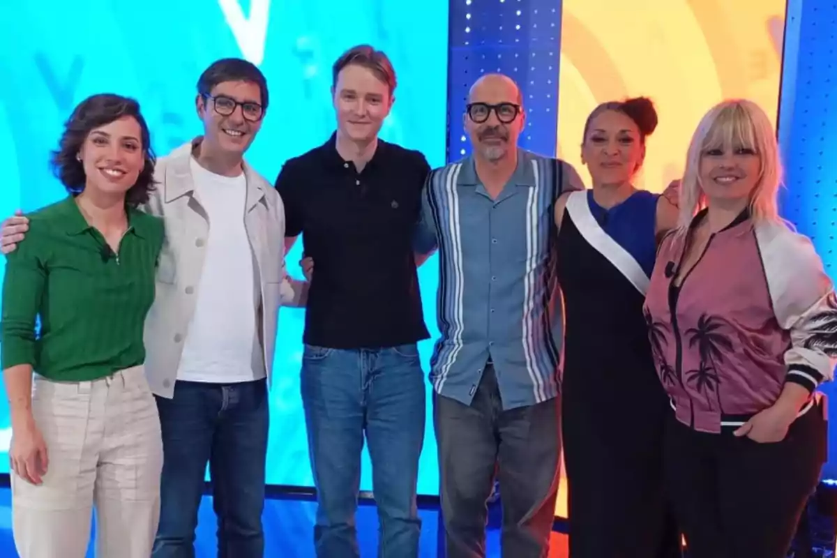 Un grupo de seis personas posando juntas en un estudio de televisión con un fondo colorido. Un grupo de seis personas posando juntas en un estudio de televisión con un fondo colorido.