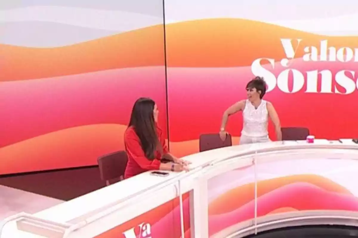 Sonsoles Ónega e Isabel Rábago conversan en un set de televisión con un fondo colorido y un escritorio curvo. Sonsoles Ónega e Isabel Rábago conversan en un set de televisión con un fondo colorido y un escritorio curvo.