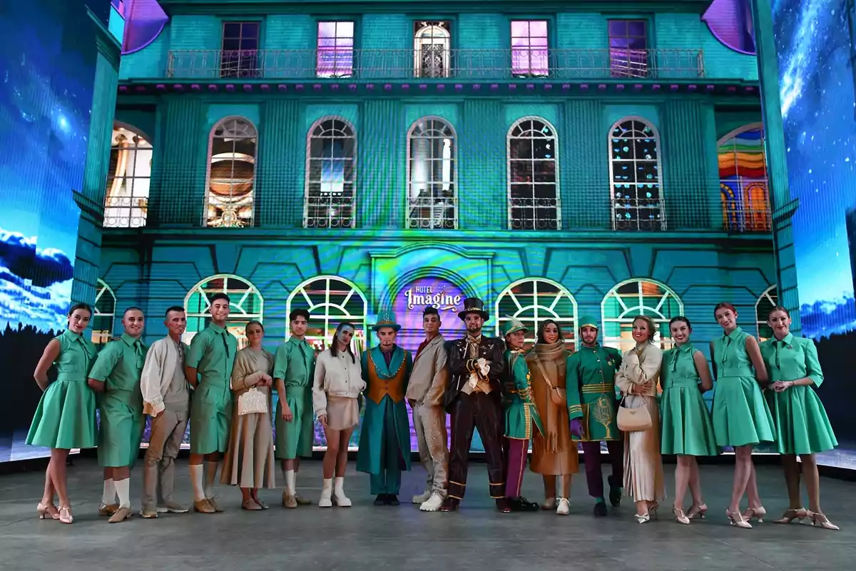 Un grupo de personas posa frente a un edificio iluminado con un letrero que dice Un grupo de personas posa frente a un edificio iluminado con un letrero que dice