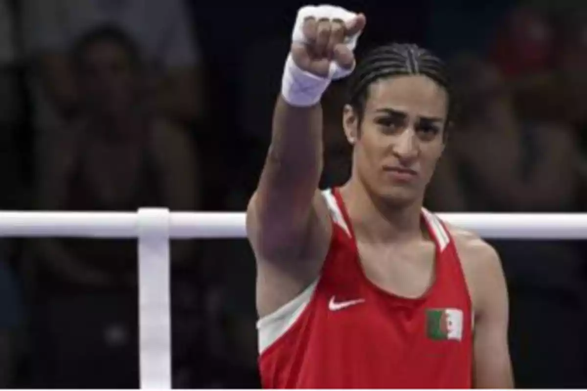 Boxeadora con uniforme rojo levantando el puño en señal de victoria dentro de un ring.