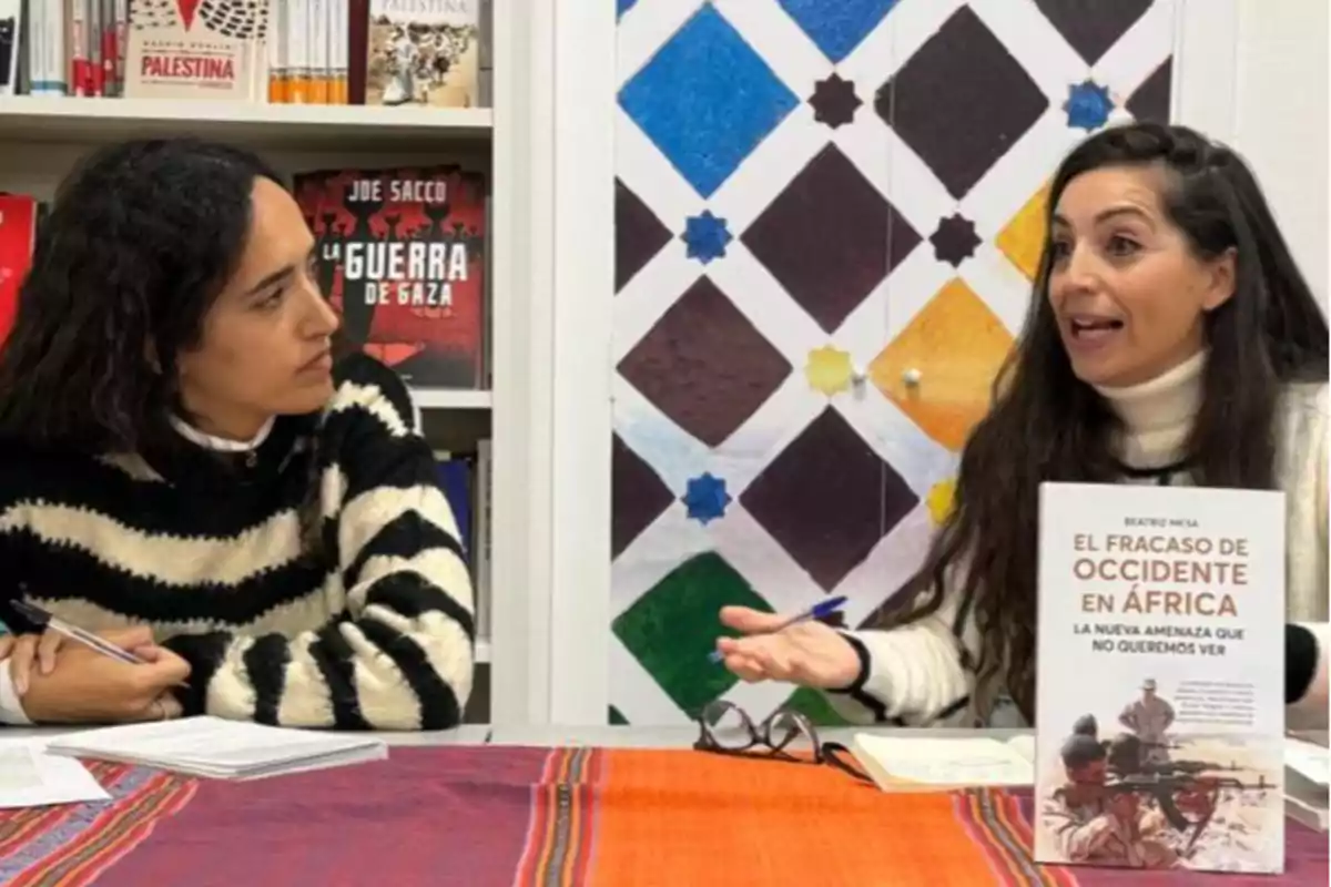 Dos mujeres conversan en una librería, una de ellas sostiene un libro titulado "El fracaso de Occidente en África".