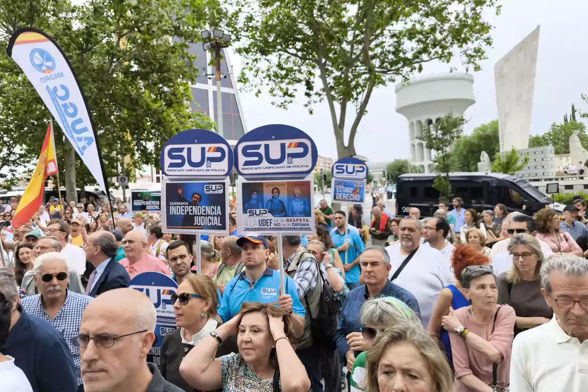 Manifestación con muchas personas en la calle sosteniendo pancartas del Sindicato Unificado de Policía y banderas, en un entorno urbano con árboles y edificios al fondo