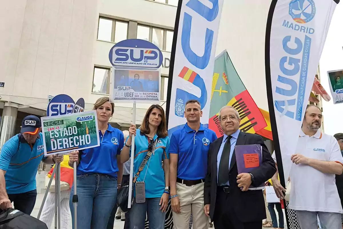 Varias personas posan en una manifestación con pancartas y banderas de sindicatos policiales frente a un edificio Varias personas posan en una manifestación con pancartas y banderas de sindicatos policiales frente a un edificio