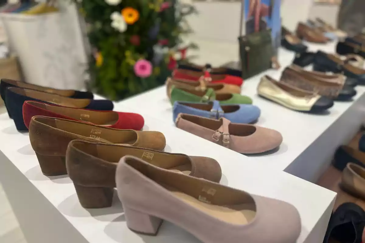 Zapatos de diferentes colores y estilos exhibidos en una tienda sobre una mesa blanca con un fondo de flores. Zapatos de diferentes colores y estilos exhibidos en una tienda sobre una mesa blanca con un fondo de flores.