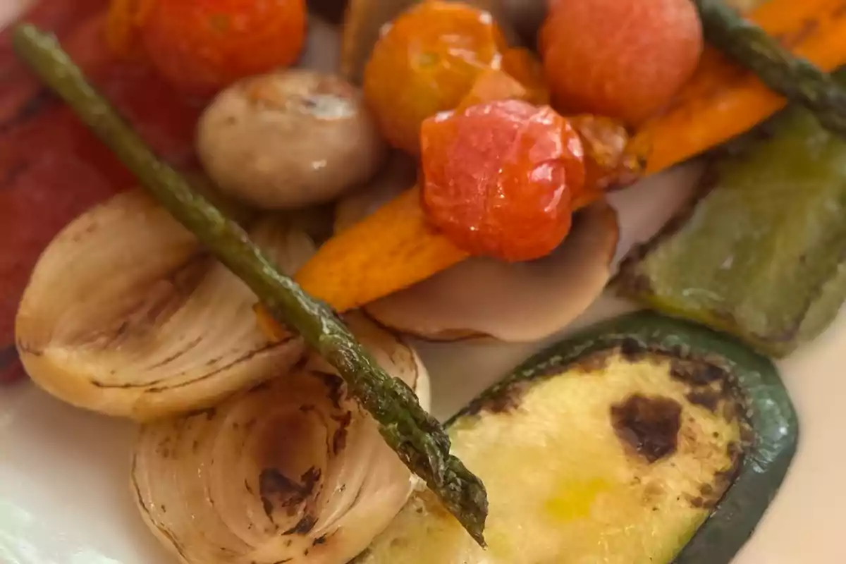 Un plato de verduras asadas que incluye espárragos, cebolla, calabacín, pimientos, champiñones, zanahorias y tomates cherry. Un plato de verduras asadas que incluye espárragos, cebolla, calabacín, pimientos, champiñones, zanahorias y tomates cherry.