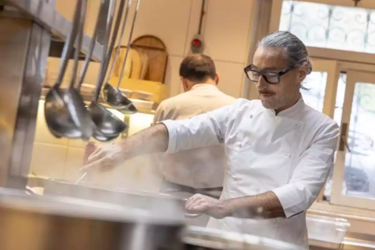 Chef cocinando en una cocina profesional con cucharones colgados en primer plano.