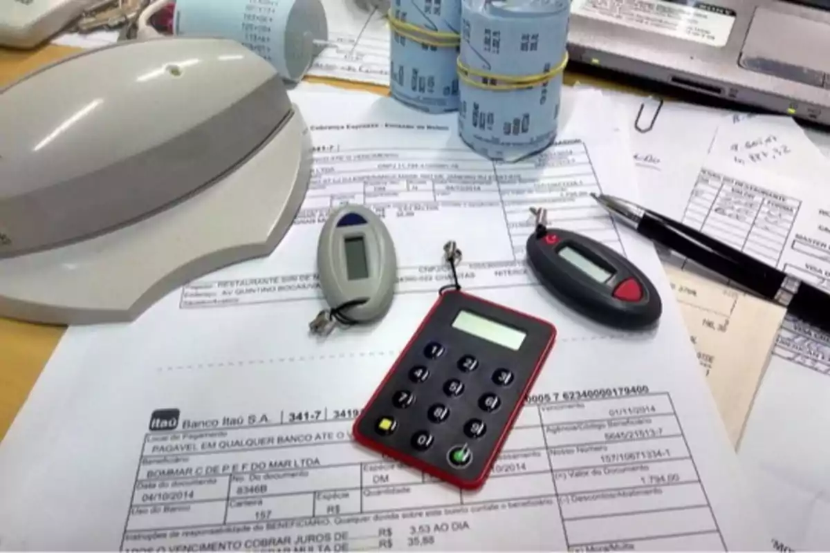 Dispositivos de seguridad bancaria, recibos, bolígrafo y una computadora portátil sobre una mesa de oficina