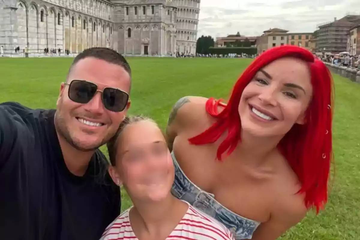 Una familia sonriente posa para una selfie frente a la Torre de Pisa en un día nublado.