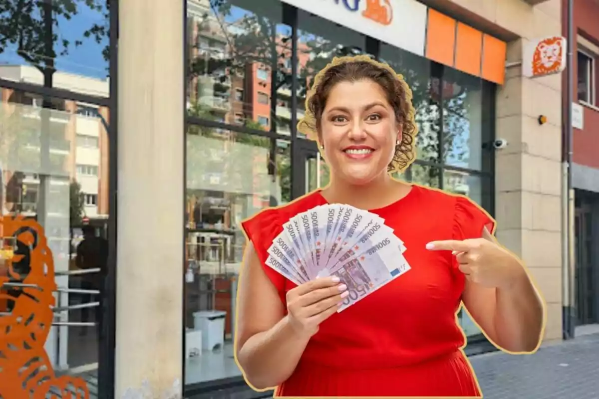 Una mujer sonriente con un vestido rojo sostiene varios billetes de 500 euros frente a una sucursal bancaria.