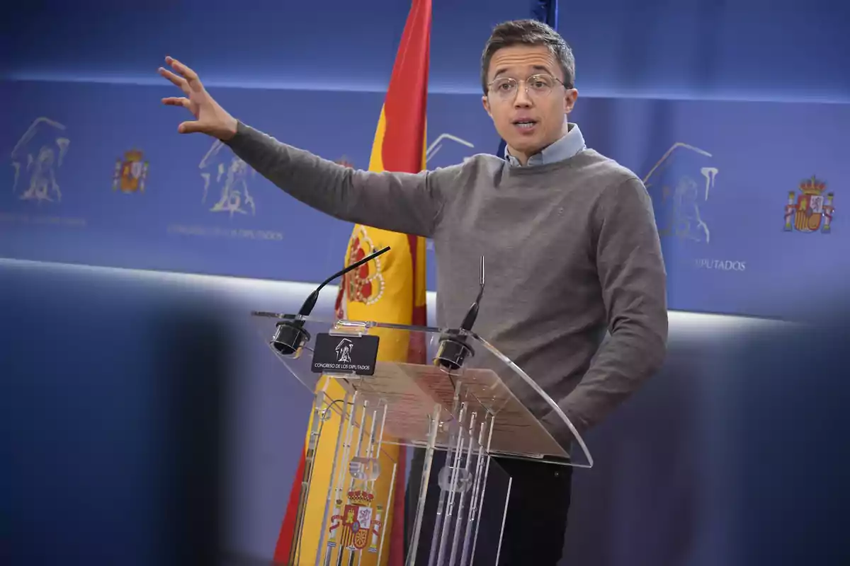 Un hombre hablando en un podio con banderas de España y un fondo azul.