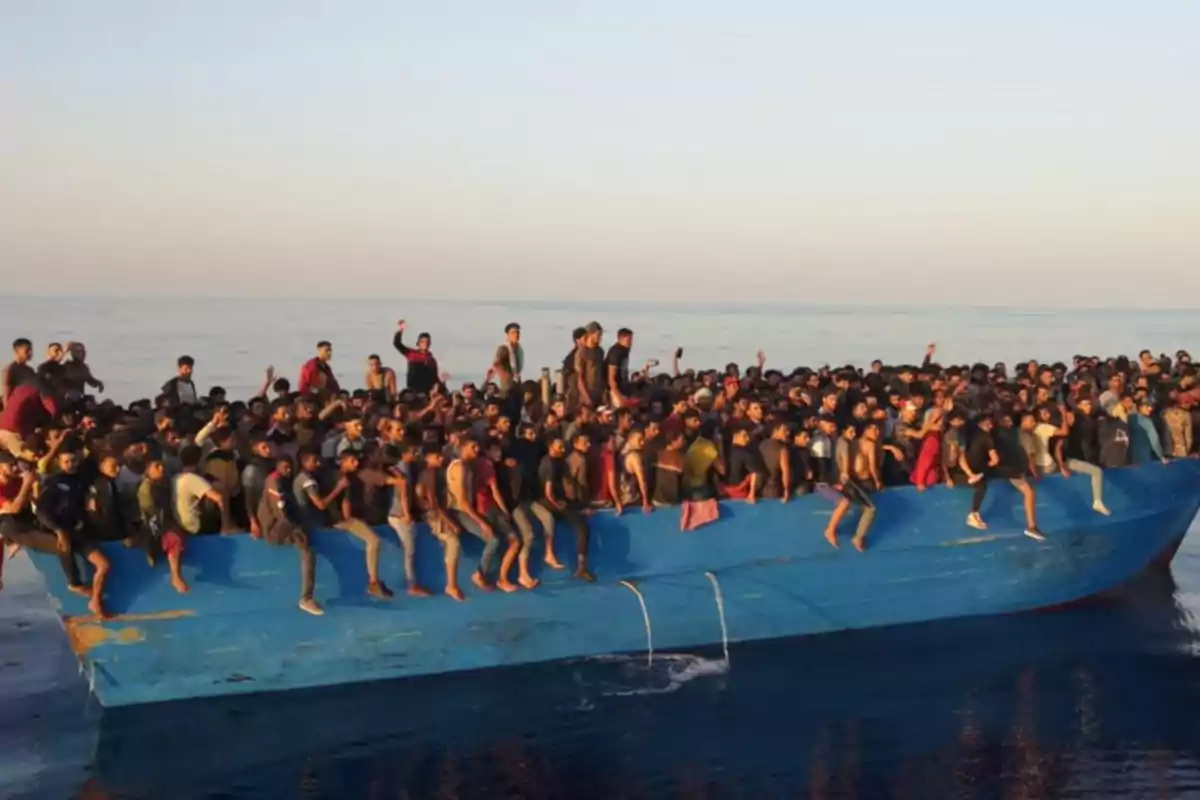 Un barco azul sobrecargado de personas en el mar.