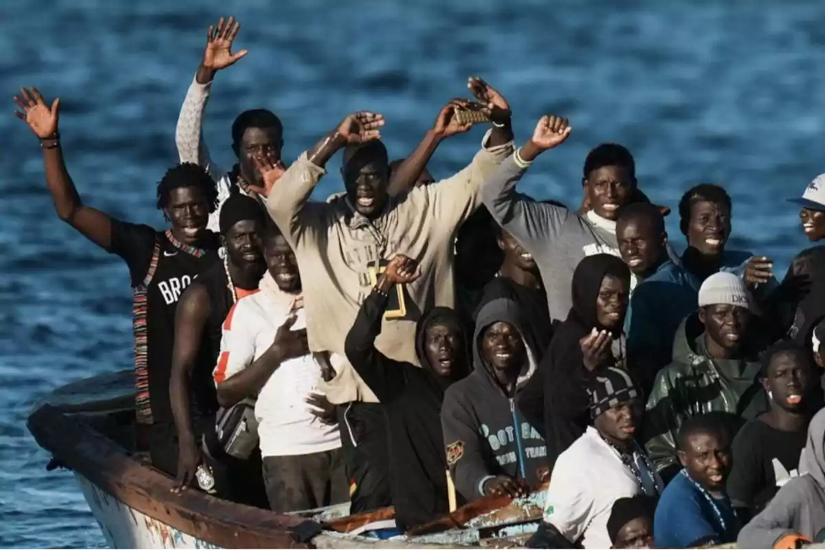 Un grupo de personas en un bote en el mar, algunas levantando los brazos y sonriendo.