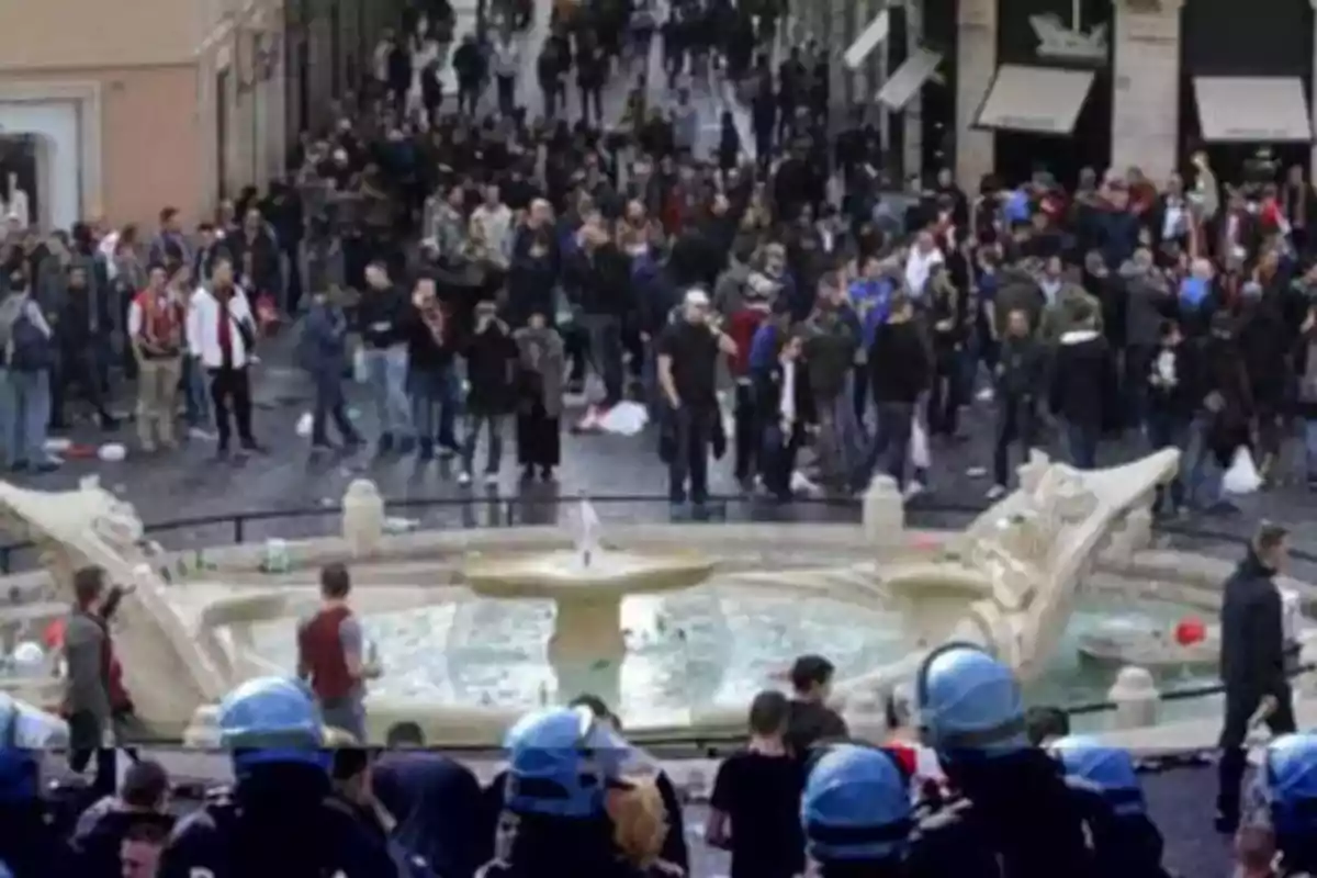 Una multitud de personas se reúne alrededor de una fuente en una plaza, mientras varios policías con cascos azules observan la escena.