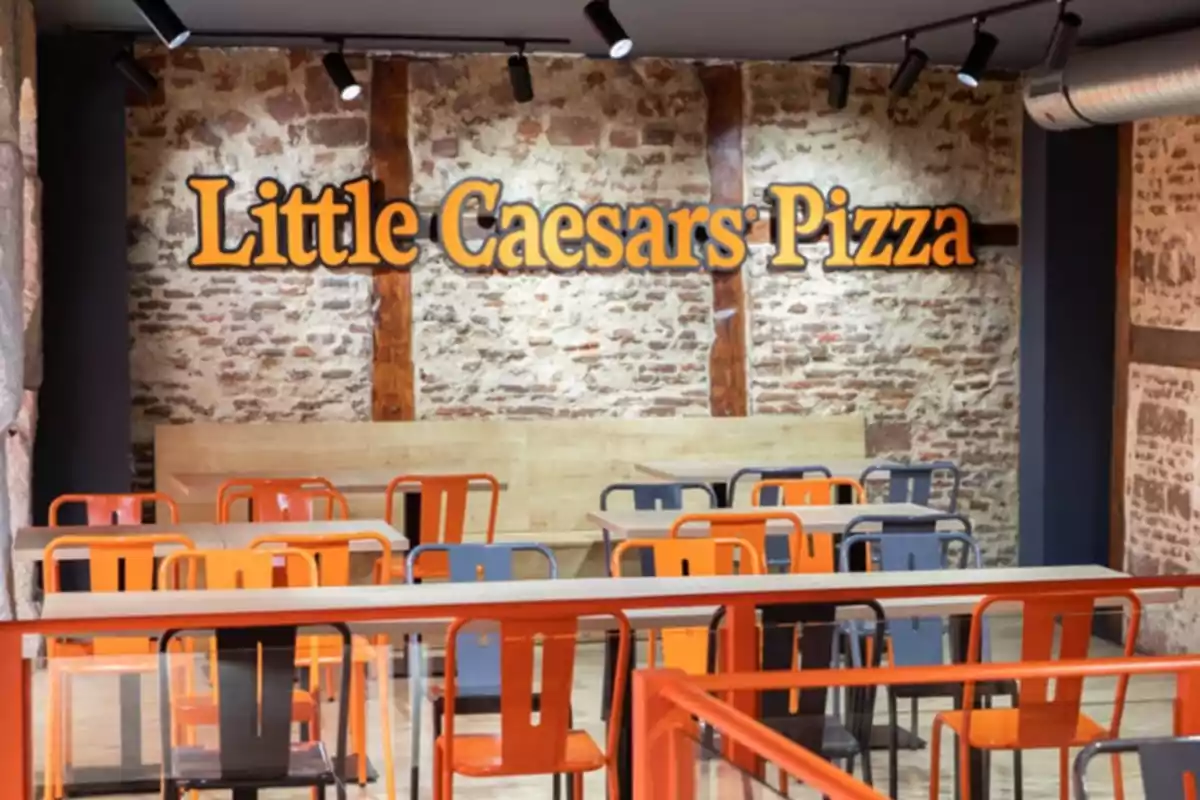 Un restaurante de pizza con sillas naranjas y grises frente a una pared de ladrillo. Un restaurante de pizza con sillas naranjas y grises frente a una pared de ladrillo.