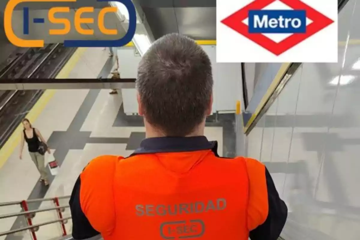 Un guardia de seguridad con chaleco naranja de espaldas en una estación de metro, con logotipos de I-SEC y Metro visibles.