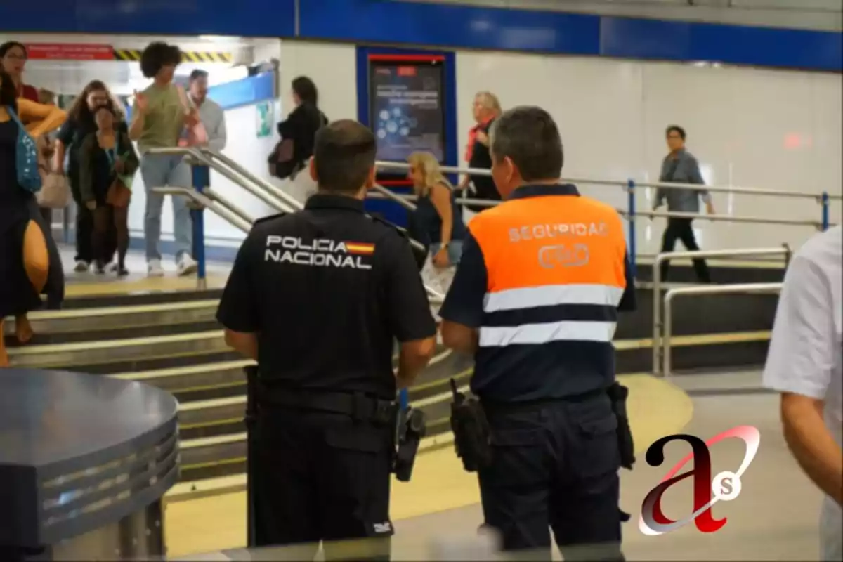 Dos agentes de seguridad, uno de la Policía Nacional y otro de seguridad privada, observan a las personas que transitan por una estación.