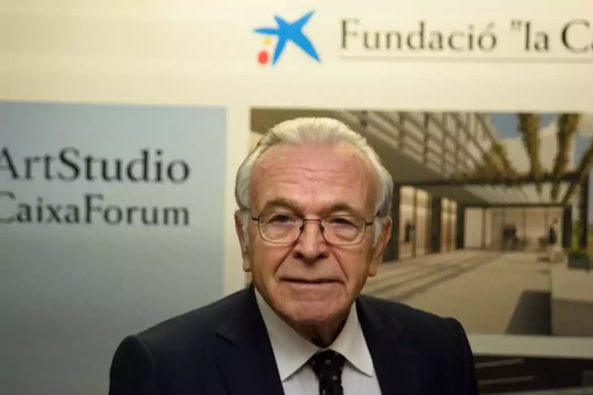 Un hombre mayor con gafas y traje oscuro está frente a un cartel que dice "Fundació la Caixa" y "ArtStudio CaixaForum".