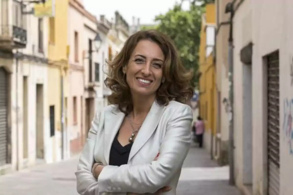 Mujer sonriendo con chaqueta blanca en una calle estrecha con edificios coloridos.