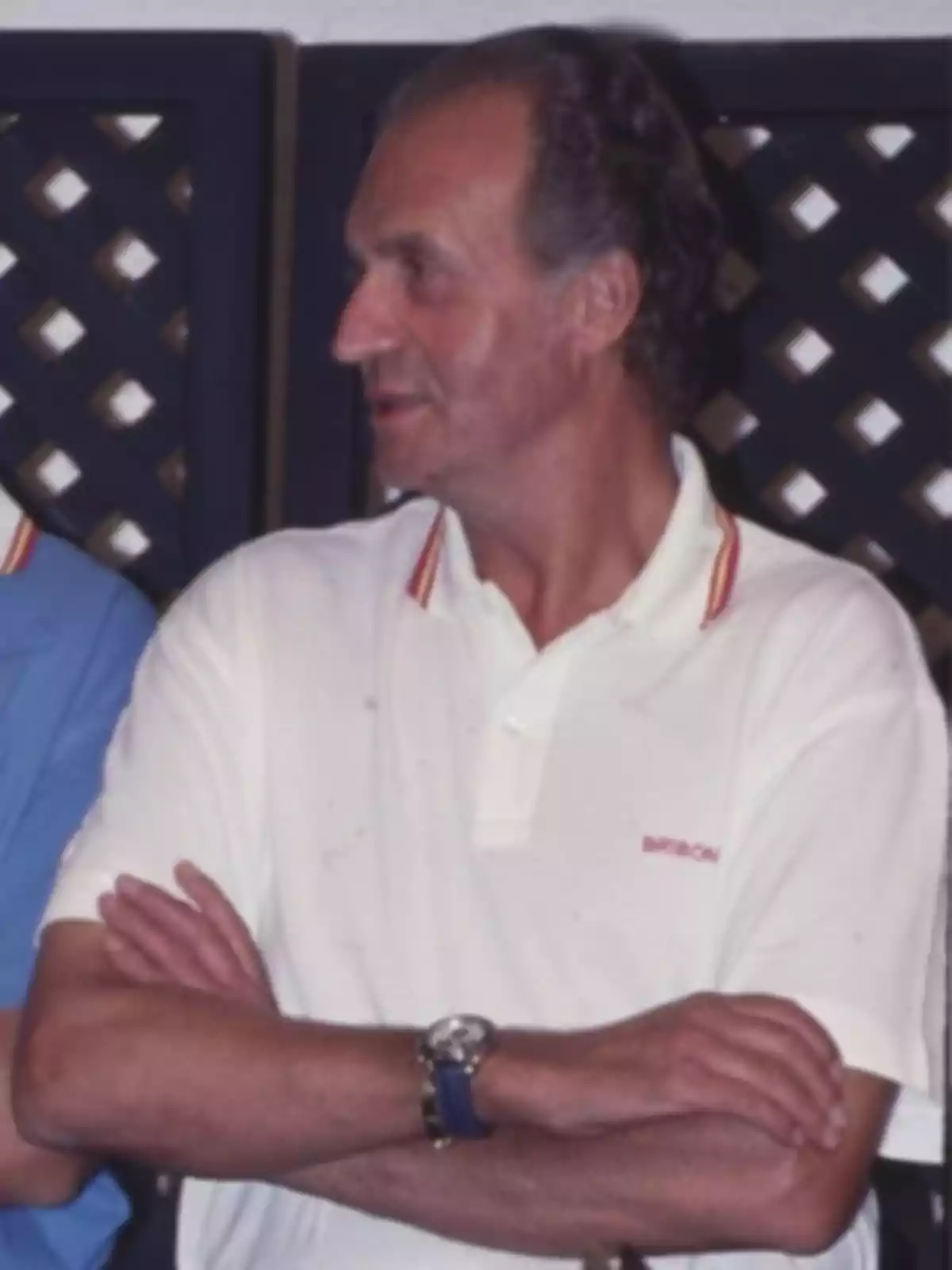 Hombre de mediana edad con cabello corto y canoso viste una camiseta polo blanca con detalles en el cuello y lleva los brazos cruzados Hombre de mediana edad con cabello corto y canoso viste una camiseta polo blanca con detalles en el cuello y lleva los brazos cruzados