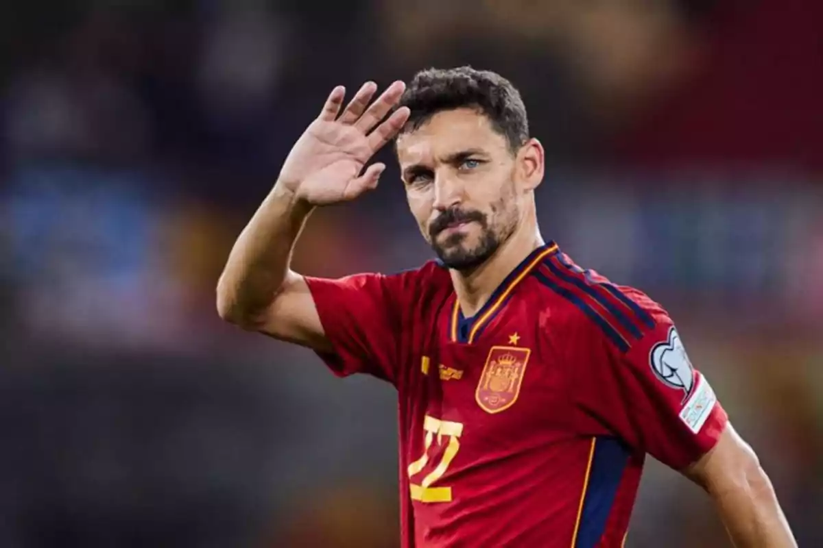 Un jugador de fútbol con uniforme rojo saluda levantando la mano.