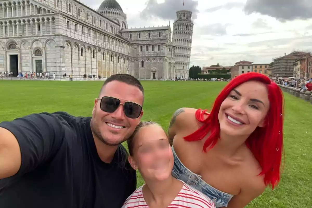Una familia sonriente se toma una selfie frente a la Torre de Pisa en un día nublado.