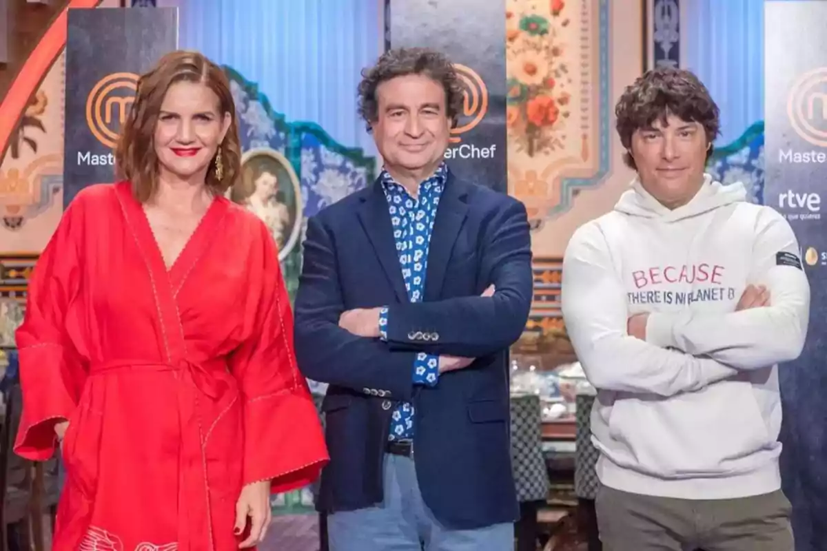 Tres personas posan frente a un fondo decorado con el logotipo de MasterChef, una de ellas lleva un vestido rojo, otra un traje azul y la tercera una sudadera blanca con un mensaje ambiental.