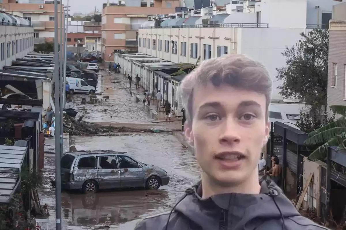 Un joven con chaqueta oscura aparece en primer plano mientras al fondo se observa una calle inundada con varios vehículos y personas limpiando los escombros.