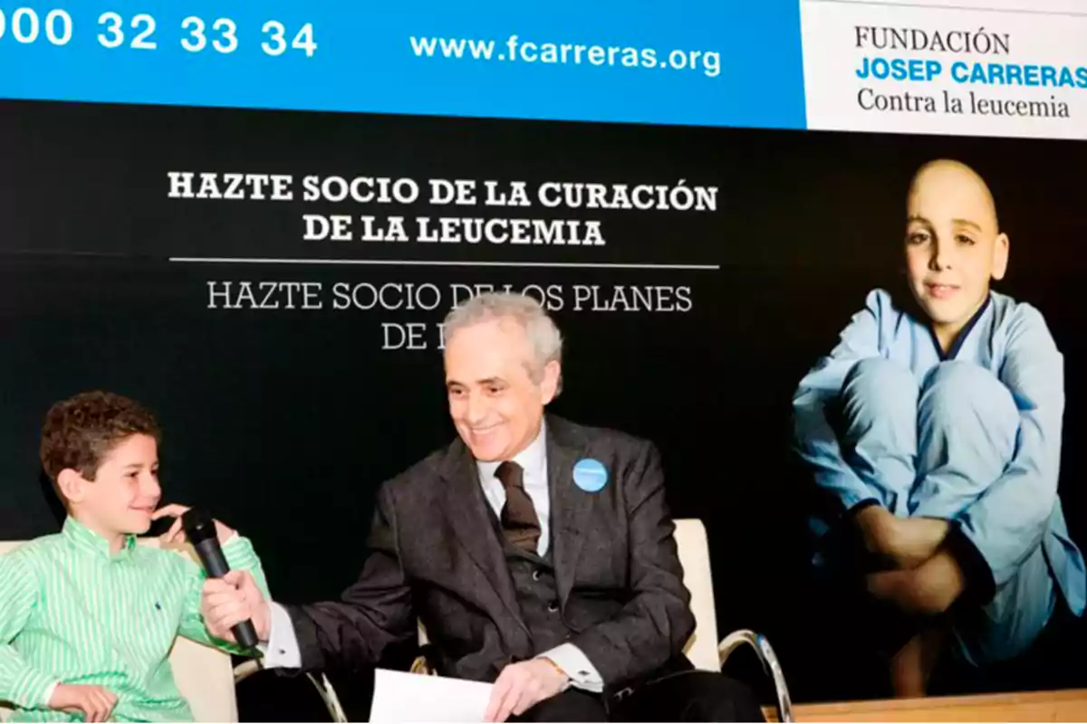 Un hombre mayor sonríe mientras sostiene un micrófono frente a un niño en un evento de la Fundación Josep Carreras contra la leucemia. Un hombre mayor sonríe mientras sostiene un micrófono frente a un niño en un evento de la Fundación Josep Carreras contra la leucemia.