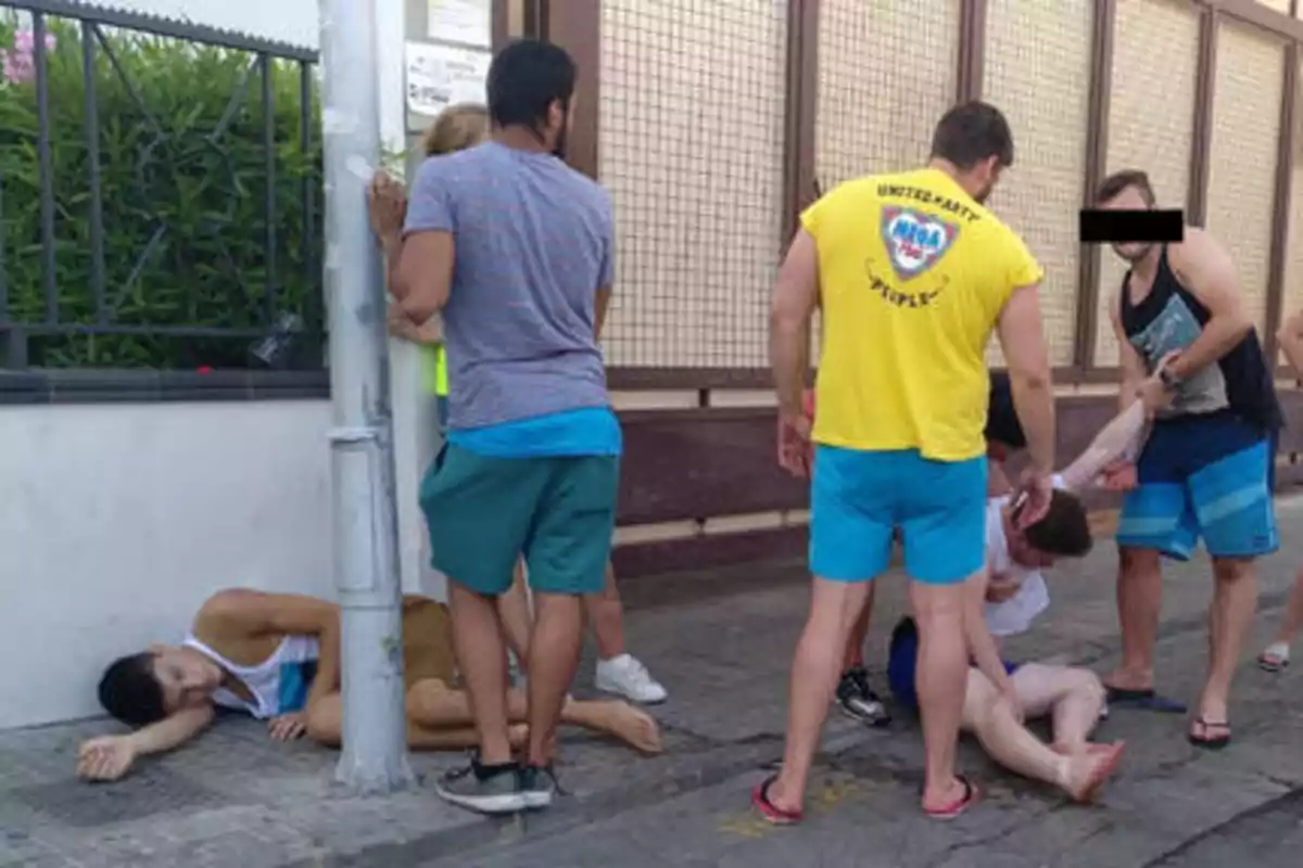 Un grupo de personas ayuda a dos individuos que parecen estar en el suelo en una calle.