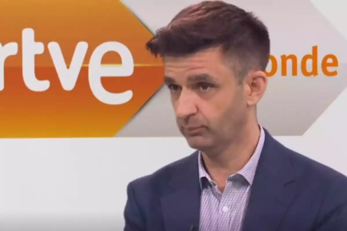 Un hombre con traje oscuro y camisa clara está en un estudio de televisión con el logo de RTVE en el fondo.