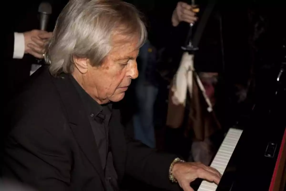 Un hombre mayor tocando el piano en un ambiente oscuro y elegante.