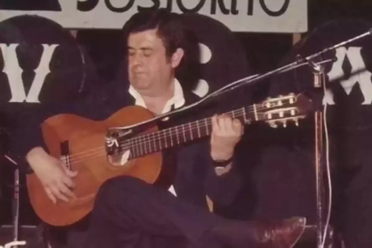 Hombre tocando una guitarra española en un escenario con un micrófono frente a él