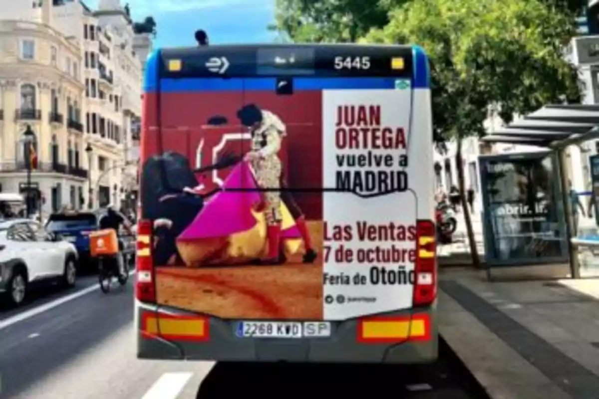 La imagen muestra la parte trasera de un autobús en una calle de Madrid, con un anuncio de una corrida de toros protagonizada por Juan Ortega, que se llevará a cabo en Las Ventas el 7 de octubre durante la Feria de Otoño.