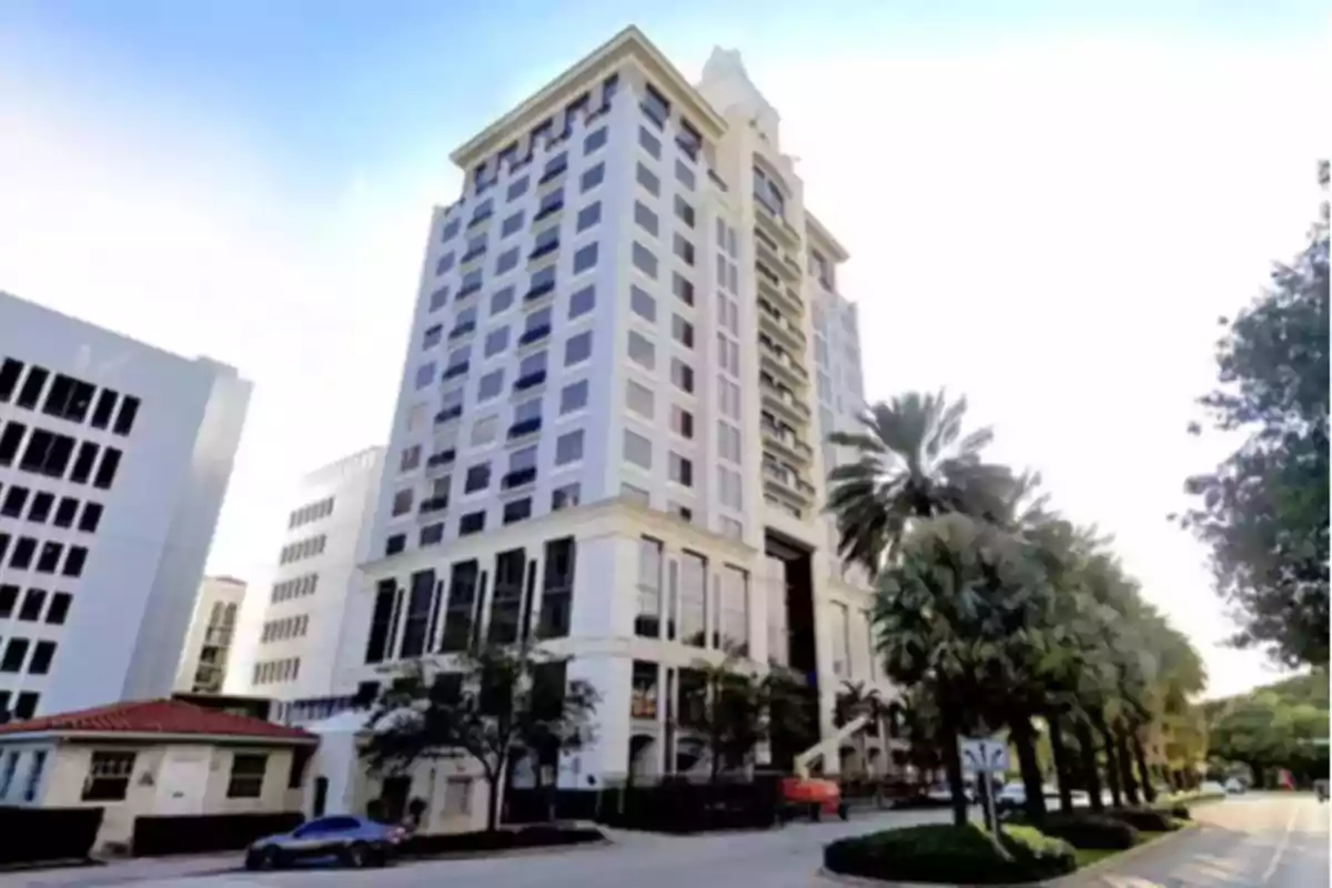 Un edificio alto con múltiples ventanas rodeado de palmeras y una calle. Un edificio alto con múltiples ventanas rodeado de palmeras y una calle.
