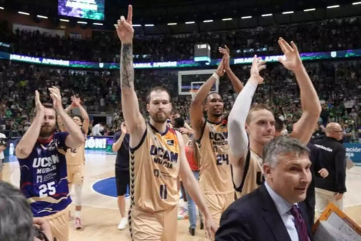 Jugadores de baloncesto del equipo UCAM Murcia celebran en la cancha mientras el público aplaude en el fondo.