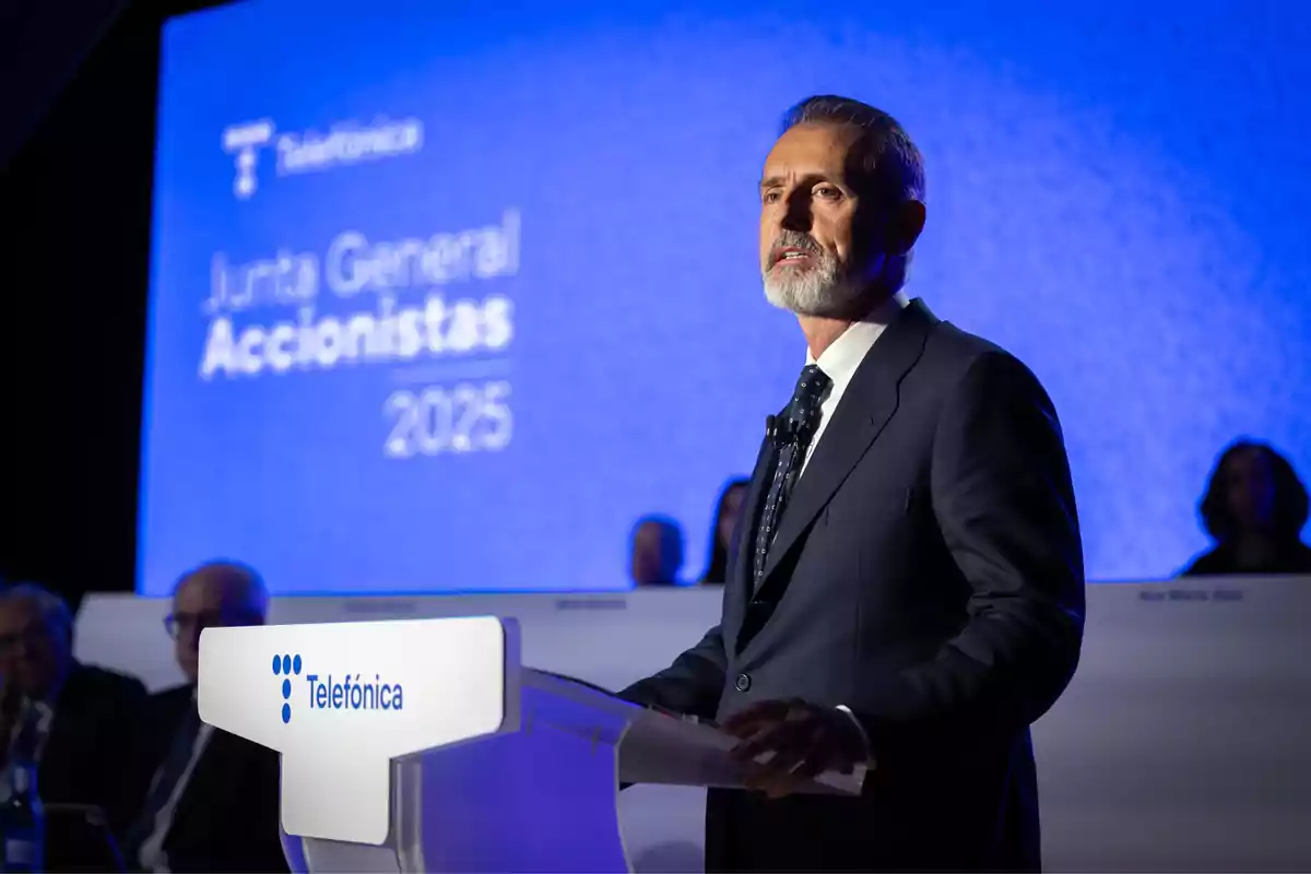Hombre de traje hablando en un podio de Telefónica durante una junta general de accionistas con fondo azul y texto de 2025.