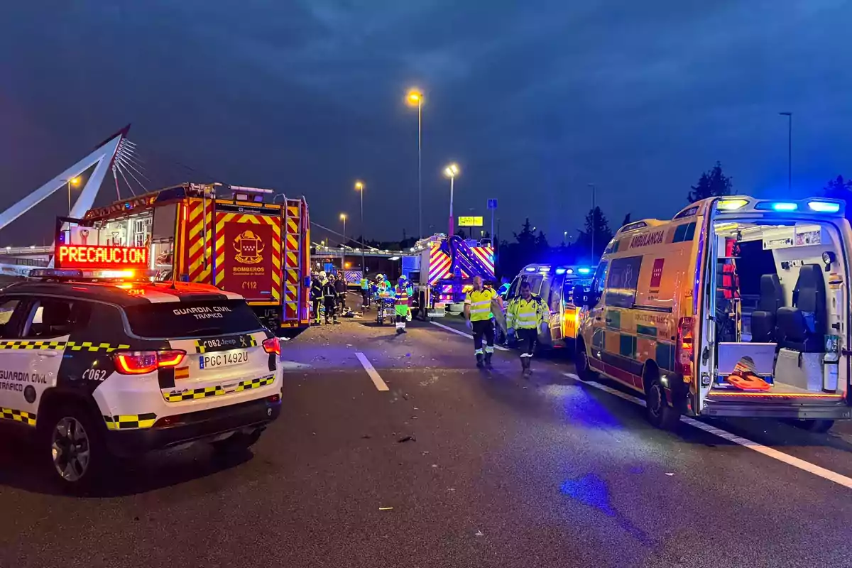 Accidente de tráfico en una carretera con presencia de vehículos de emergencia, incluyendo ambulancias, bomberos y la Guardia Civil, durante la noche.