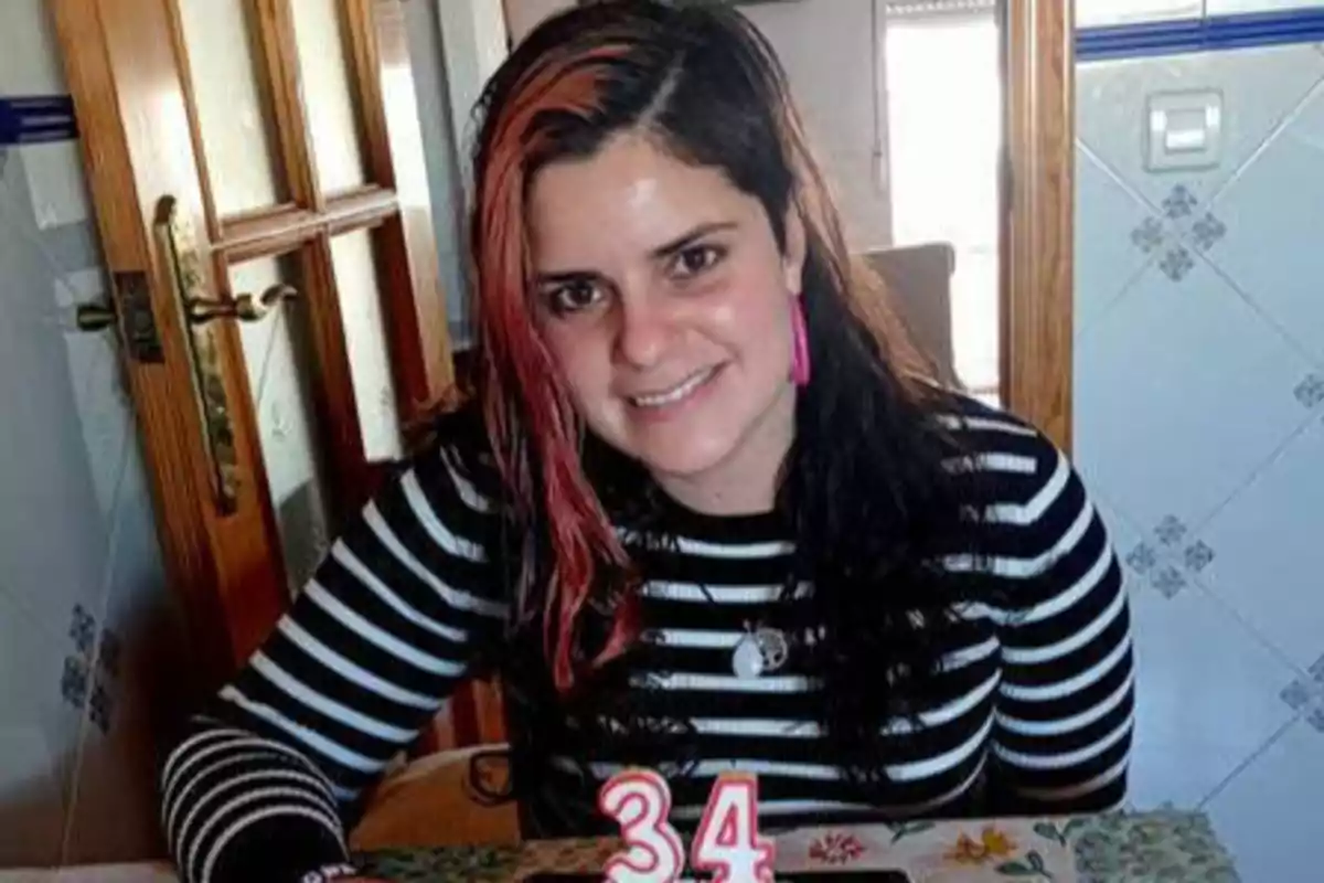 Mujer sonriendo con camiseta de rayas negras y blancas, sentada frente a una mesa con velas de cumpleaños que forman el número 34.