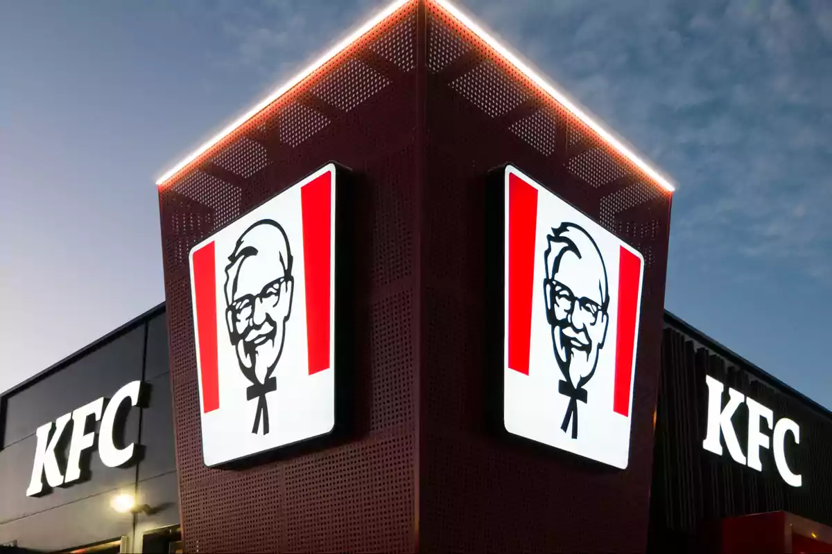 Un edificio de KFC con el logotipo iluminado en la fachada al anochecer. Un edificio de KFC con el logotipo iluminado en la fachada al anochecer.