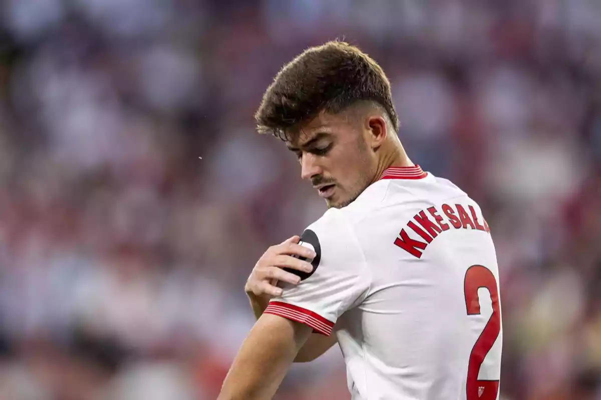 Un jugador de fútbol con camiseta blanca y el número 2 en la espalda ajustándose la manga en un estadio.