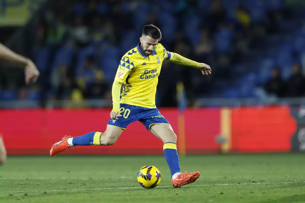 Un jugador de fútbol con uniforme amarillo y azul patea un balón en un estadio durante un partido. Un jugador de fútbol con uniforme amarillo y azul patea un balón en un estadio durante un partido.