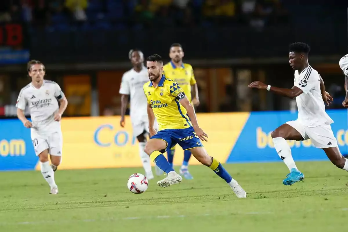 Jugadores de fútbol en acción durante un partido, uno con uniforme amarillo y azul y otros con uniforme blanco. Jugadores de fútbol en acción durante un partido, uno con uniforme amarillo y azul y otros con uniforme blanco.
