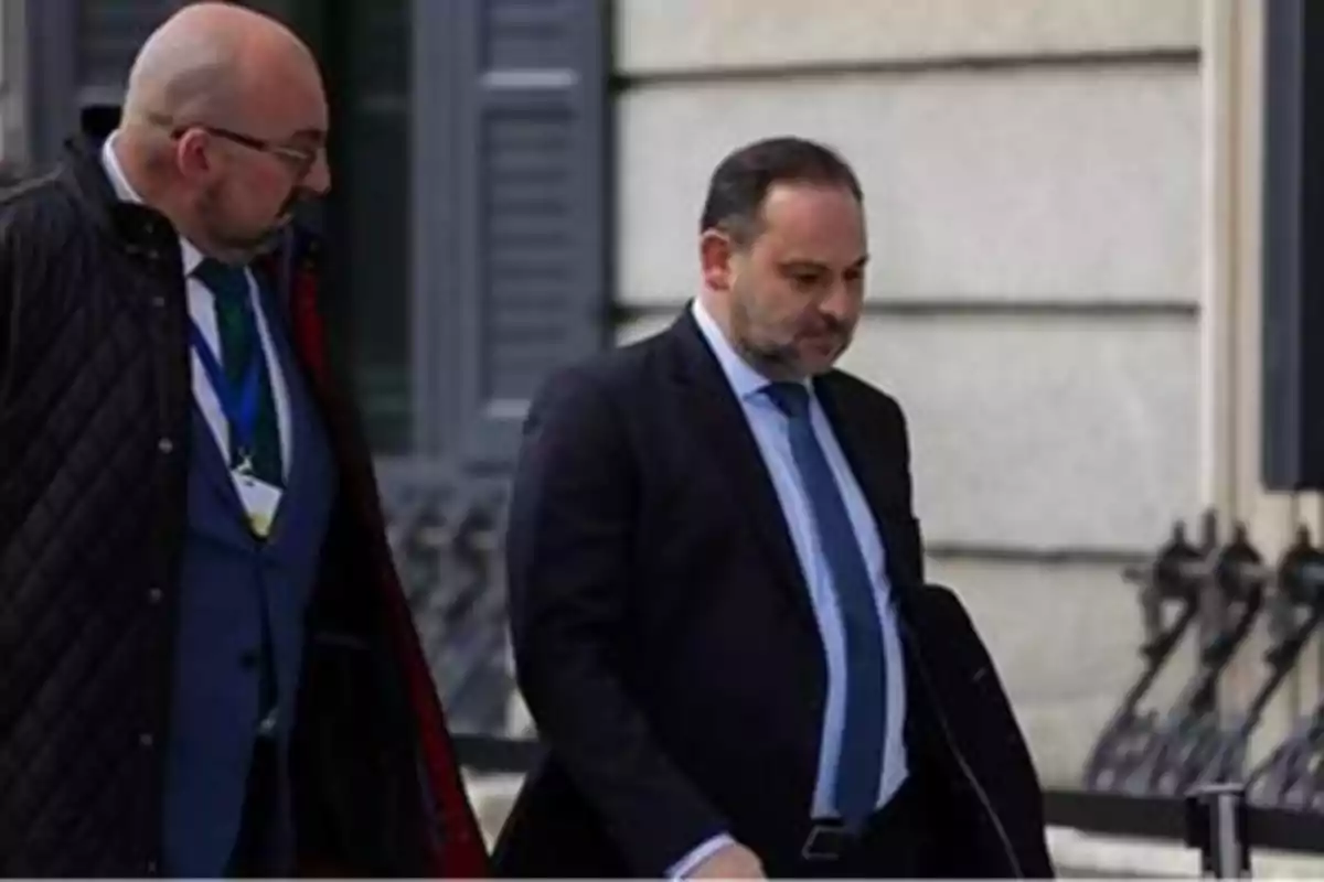 Dos hombres caminando juntos con trajes formales frente a un edificio.