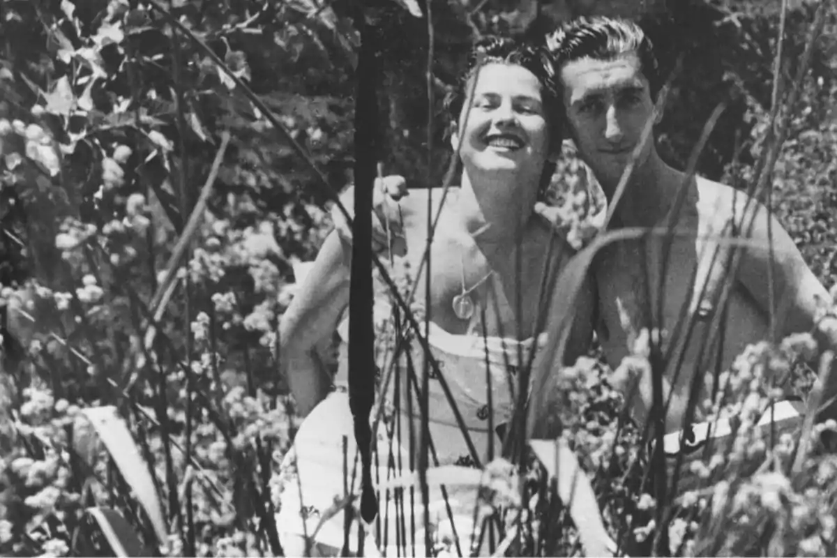 Una pareja sonriente posando juntos en un jardín lleno de vegetación y flores.